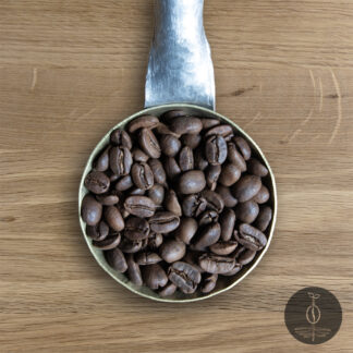 Close-up shot of Decaf Peru Cajamarca light roasted coffee beans in a handmade scoop with a wooden cutting board background.