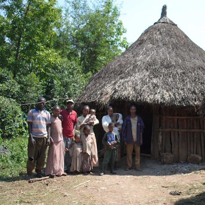Coffee farming family in Ethiopia standing beside their home made of wood with a grass roof