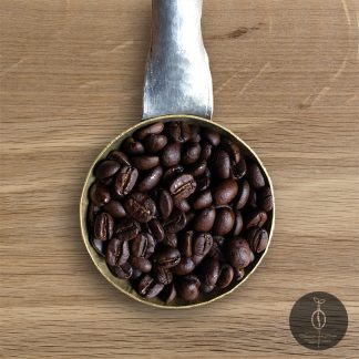 Close-up shot of Bolivia Yungas Mountain dark roasted coffee beans in a handmade scoop with a wooden cutting board background.