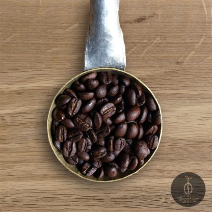 Close-up shot of Bolivia Yungas Mountain dark roasted coffee beans in a handmade scoop with a wooden cutting board background.