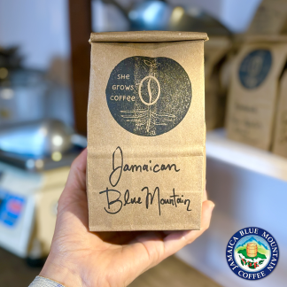 Product Shot: Recycled kraft bag filled with fresh roasted coffee, labelled "Jamaican Blue Mountain", branded with a She Grows Coffee stamp.