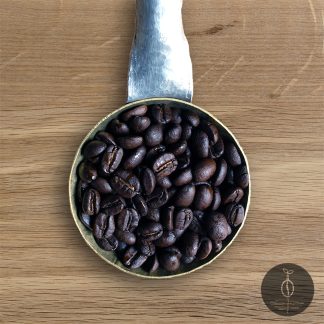 Close-up shot of Bolivia Yungas Mountain dark roasted coffee beans in a handmade scoop with a wooden cutting board background.