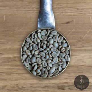 Close-up shot of Colombia Sierra Nevada green (raw) coffee beans in a handmade scoop with a wooden cutting board background.