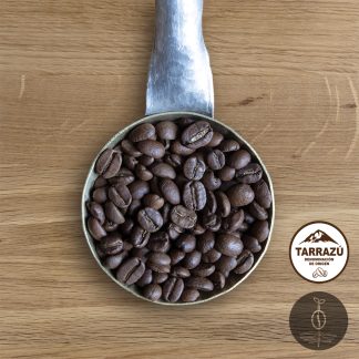 Close-up shot of Costa Rica La Pastora medium roasted coffee beans in a handmade scoop with a wooden cutting board background.