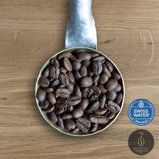 Close-up shot of Decaf Peru Cajamarca light roasted coffee beans in a handmade scoop with a wooden cutting board background.