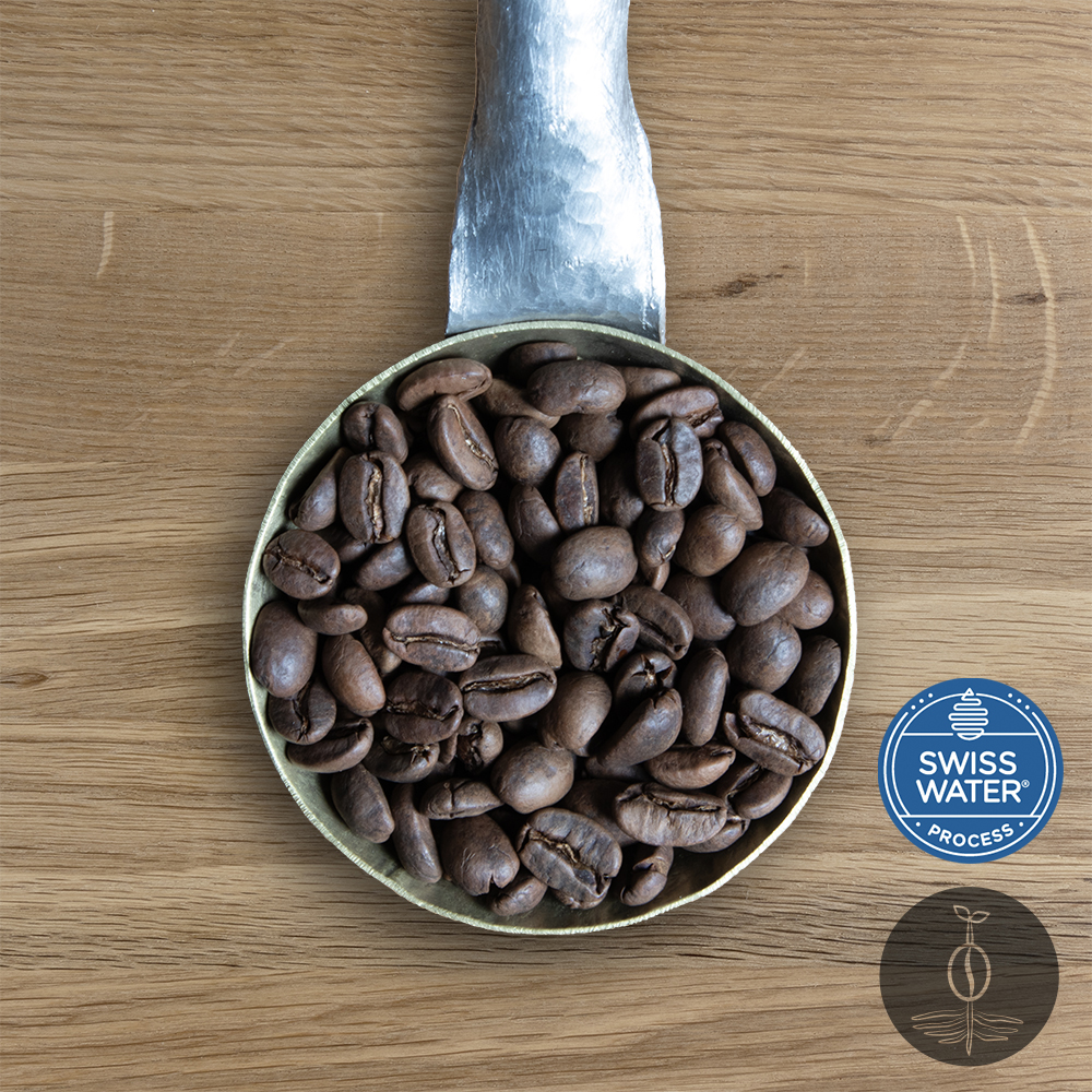 Close-up shot of Decaf Peru Cajamarca light roasted coffee beans in a handmade scoop with a wooden cutting board background.