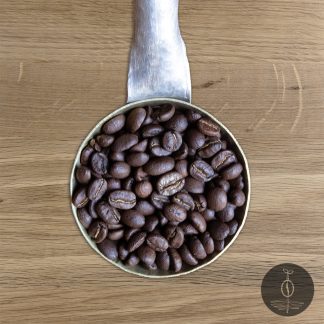 Close-up shot of Guatemala San Marcos medium roasted coffee beans in a handmade scoop with a wooden cutting board background.