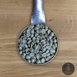 Close-up shot of Guatemala San Marcos green (raw) coffee beans in a handmade scoop with a wooden cutting board background.