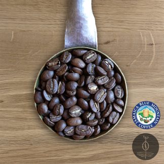Close-up shot of Jamaica Blue Mountain Clydesdale Estate Grade light-medium roasted coffee beans in a handmade scoop with a wooden cutting board background.