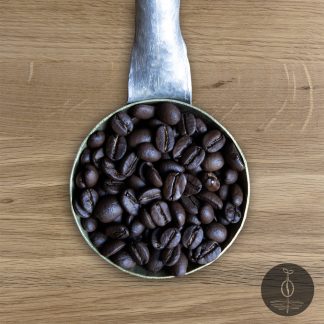 Close-up shot of Mexico Chiapas dark roasted coffee beans in a handmade scoop with a wooden cutting board background.
