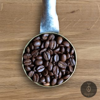 Close-up shot of Papua New Guinea Korgua Estate AA medium roasted coffee beans in a handmade scoop with a wooden cutting board background.