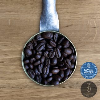 Close-up shot of Decaf Peru Cajamarca light roasted coffee beans in a handmade scoop with a wooden cutting board background.
