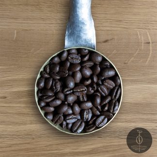 Close-up shot of Rwanda Kigayo dark roasted coffee beans in a handmade scoop with a wooden cutting board background.