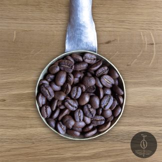Close-up shot of Sumatra Gayo Mountain medium roasted coffee beans in a handmade scoop with a wooden cutting board background.