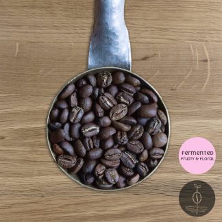 Close-up shot of Colombia Huila Geisha, La Villa light-medium roasted coffee beans in a handmade scoop with a wooden cutting board background.