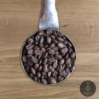 Close-up shot of Ethiopia Yirgacheffe Kochere Region light roasted coffee beans in a handmade scoop with a wooden cutting board background.