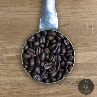 Close-up shot of Sumatra Gayo Mountain dark roasted coffee beans in a handmade scoop with a wooden cutting board background.