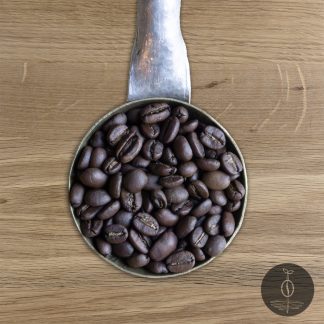 Close-up shot of Wild Leopard Blend medium roasted coffee beans in a handmade scoop with a wooden cutting board background.