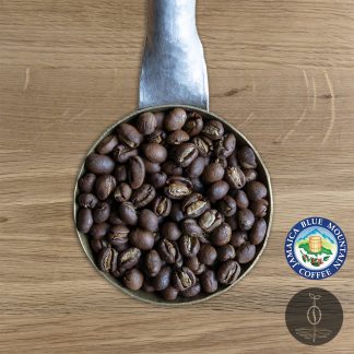 Close-up shot of Jamaica Blue Mountain, Clydesdale Peaberry light-medium roasted coffee beans in a handmade scoop with a wooden cutting board background.